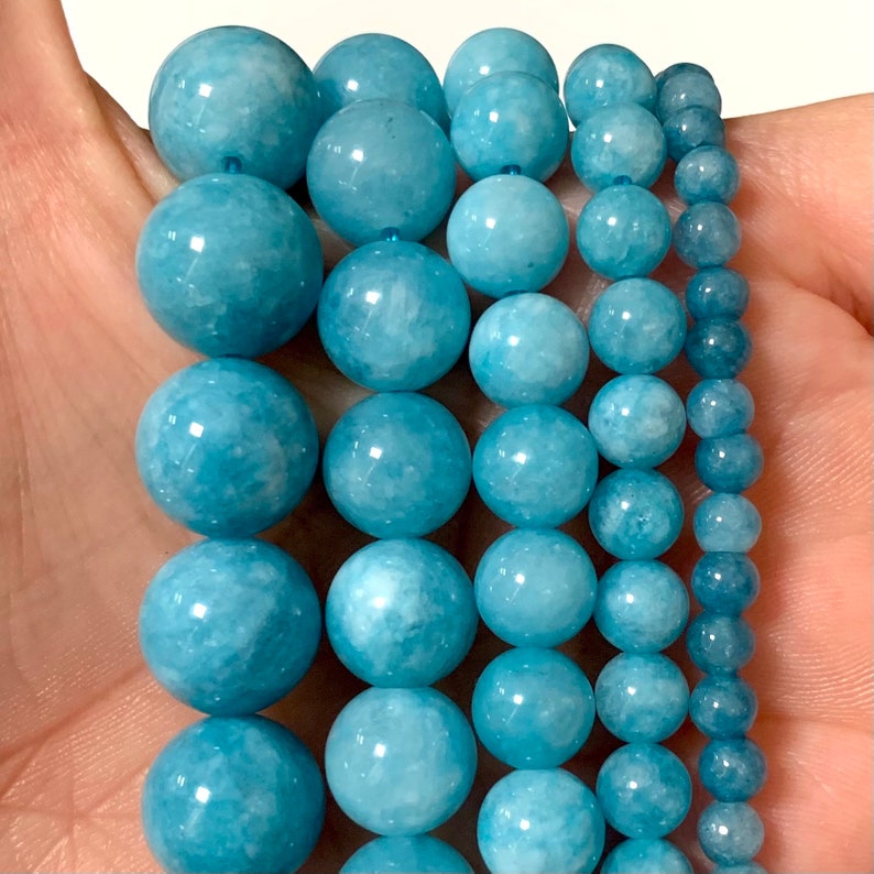 May include: A strand of light blue aquamarine beads in various sizes. The beads are round and smooth, with a slightly cloudy appearance.
