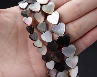 May include: A strand of heart-shaped beads made from black and white mother of pearl. The beads are strung on a clear elastic cord.