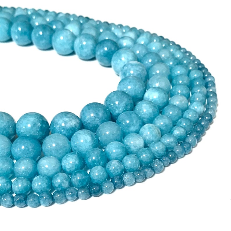 May include: A strand of light blue aquamarine beads of varying sizes. The beads are round and smooth, and they are arranged in a circle.
