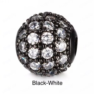 May include: Black and white round bead with a small hole for stringing. The bead is covered in small white rhinestones.