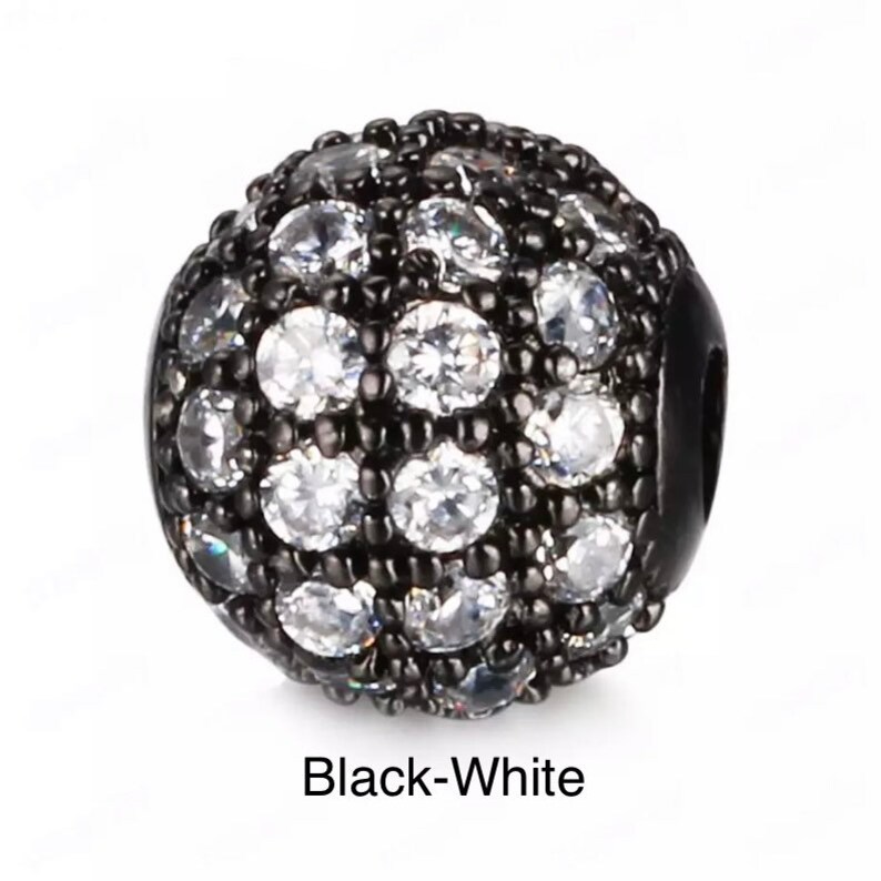 May include: Black and white round bead with a small hole for stringing. The bead is covered in small white rhinestones.