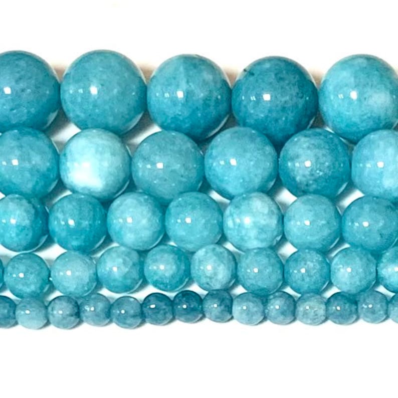 May include: A strand of light blue aquamarine beads in various sizes. The beads are round and smooth, with a slightly cloudy appearance.