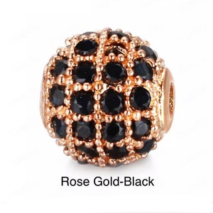 May include: A rose gold and black round bead with a geometric design. The bead is covered in small black stones.
