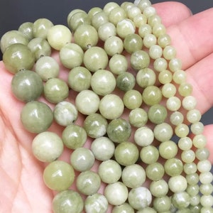 May include: A strand of light green jade beads, with a smooth, polished finish. The beads are round and uniform in size, and they are strung on a clear thread. The beads are arranged in a loose pile, and they are illuminated by a soft, natural light.