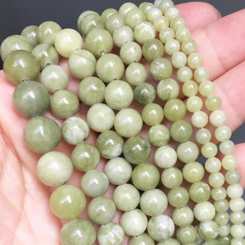 May include: A strand of light green jade beads, with a smooth, polished finish. The beads are round and uniform in size, and they are strung on a clear thread. The beads are arranged in a loose pile, and they are illuminated by a soft, natural light.