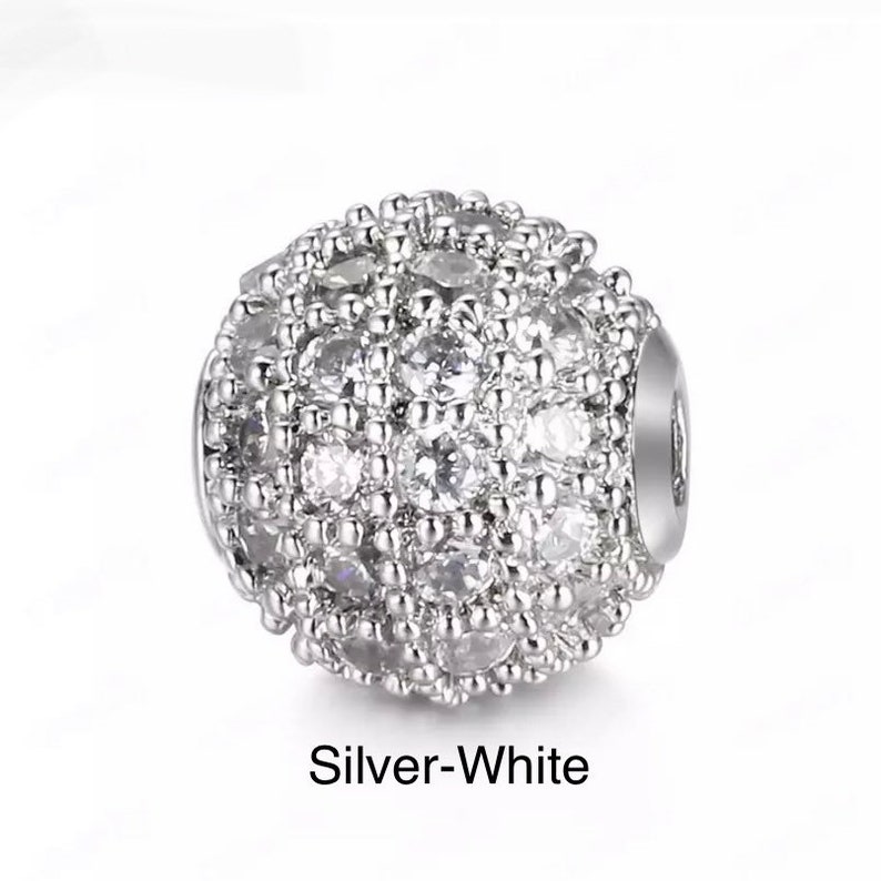 May include: A silver-toned round bead with a sparkly, white, crystal-like design. The bead is a decorative element for jewelry making.