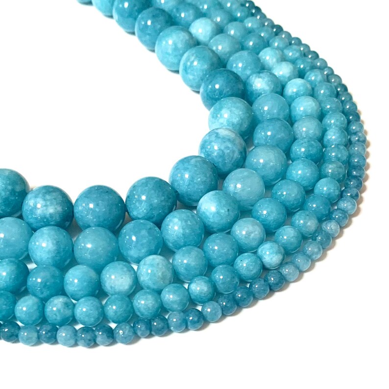 May include: A strand of round, light blue aquamarine beads of varying sizes. The beads are smooth and polished, with a subtle shimmer.