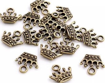 May include: A collection of small, antique bronze-colored metal crown charms. Each charm features a detailed five-point crown design with a row of small raised dots along the base and a circular jump ring attached to the top for hanging purposes.