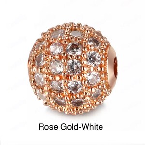 May include: A rose gold and white round bead with a pave setting of small white cubic zirconia stones.