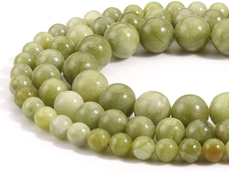 May include: A strand of light green jade beads, each bead is smooth and round. The beads are strung together on a clear thread.