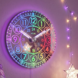 Könnte beinhalten: Eine kreisförmige Wanduhr mit einem regenbogenfarbenen LED-Rand und Ziffernblatt. Die Uhr zeigt große Zahlen von 1 bis 12 auf einem äußeren Ring, kleinere Zahlen von 13 bis 24 auf einem inneren Ring sowie Minutenmarkierungen von 0 bis 59.
