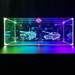Puede incluir: Una vitrina de vidrio con fondo negro y luces LED de colores. La vitrina presenta tres modelos de tanques cortados con láser, uno en el centro y dos a los lados. Los tanques están delineados en blanco y parecen flotar en el aire.