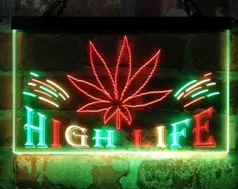 Puede incluir: Un letrero de neón rectangular con un marco negro. El letrero presenta una hoja de cannabis roja en el centro, con las palabras "HIGH LIFE" en turquesa y rojo. Rayas verdes y naranjas están a cada lado de la hoja. El letrero está colgado en una pared de ladrillos.