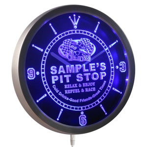 Puede incluir: Un reloj de neón azul con marco plateado. La esfera del reloj presenta un gráfico de coche de carreras y el texto "SAMPLE'S PIT STOP RELAX & ENJOY REFUEL & RACE Cold Drinks-Good Friends-Great Times".