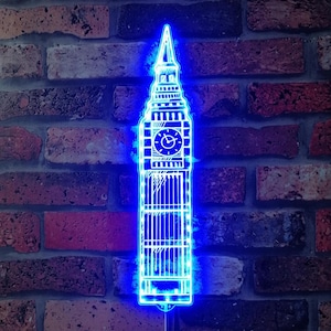 Könnte beinhalten: Ein blaues Neonlicht in Form des Big Ben, des berühmten Uhrturms in London, England. Das Licht leuchtet vor einem Hintergrund aus Ziegelmauer.