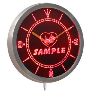 May include: Red LED clock with a silver metal frame. The clock face has a black background with a white heart and a dog silhouette inside the heart. The text "SAMPLE" is below the heart. The clock has a white cord.