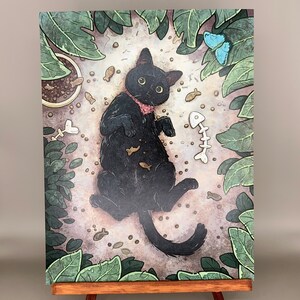 Puede incluir: Un gato negro con una pajarita rosa est&aacute; tumbado en una cama de hojas marrones y verdes. El gato est&aacute; rodeado de peque&ntilde;os huesos de pescado y otros juguetes para gatos. El gato est&aacute; mirando al espectador.