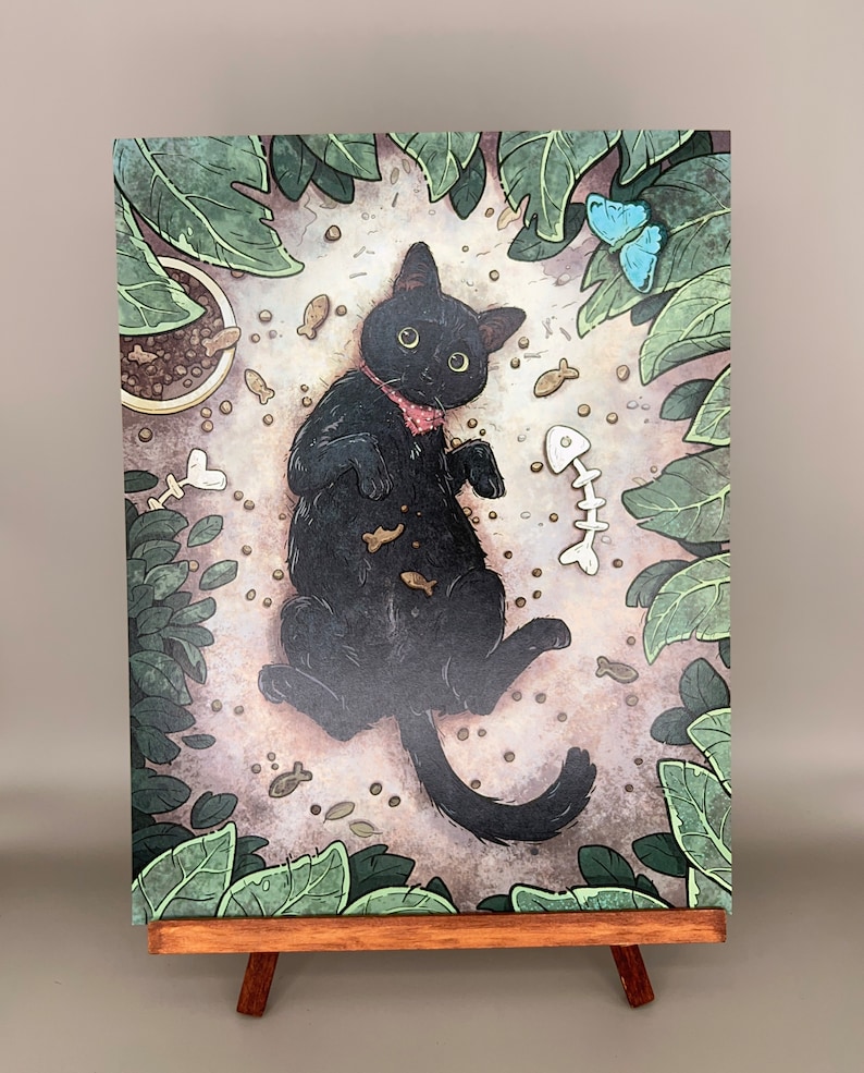 Puede incluir: Un gato negro con una pajarita rosa est&aacute; tumbado en una cama de hojas marrones y verdes. El gato est&aacute; rodeado de peque&ntilde;os huesos de pescado y otros juguetes para gatos. El gato est&aacute; mirando al espectador.