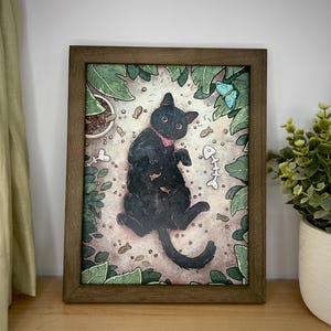 Puede incluir: Ilustraci&oacute;n enmarcada de un gato negro con un collar rosa acostado en una cama de comida para gatos marr&oacute;n rodeada de hojas verdes y mariposas.