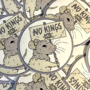 May include: A collection of round stickers featuring a cartoon rat holding a sign that reads "NO KINGS." The rat is gray and white, with a detailed illustration style. The sign has a crown with a line through it. The stickers have a gray border.