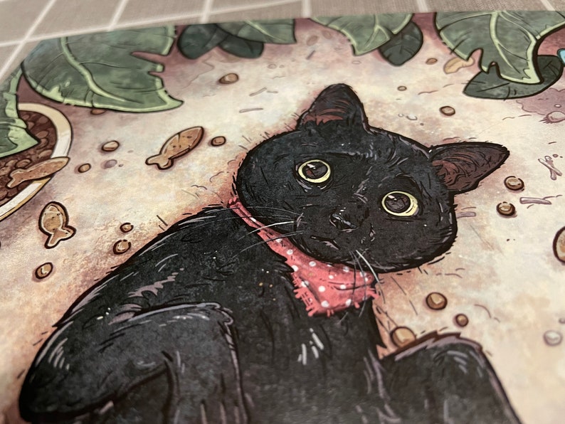 Puede incluir: Un gato negro con una pajarita de lunares rosas est&aacute; tumbado sobre una superficie marr&oacute;n claro con puntos marrones dispersos. El gato tiene ojos grandes y redondos y una expresi&oacute;n de sorpresa.