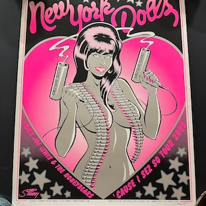Peut inclure: Une affiche rose et noire avec une illustration de bande dessinée d'une femme tenant deux bâtons de dynamite. Le texte sur l'affiche indique "New York Dolls" et "Cause I Sez So Tour 2009".