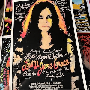 May include: A black and white concert poster featuring a portrait of Laura Jane Grace with text that reads "Two Nights With Laura Jane Grace" at The Bricks in Tampa, Florida. The poster includes show dates and venue details.