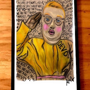 Peut inclure: Une œuvre d'art encadrée représentant un portrait stylisé d'une personne aux joues roses, portant des lunettes et une combinaison jaune avec le mot "DEVO". L'œuvre comprend du texte manuscrit.