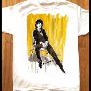 Peut inclure: T-shirt blanc avec une illustration en noir et blanc d'une personne assise sur une chaise. L'arrière-plan est jaune avec des coups de pinceau noirs. Le texte "So Alone" est écrit en noir sous la personne.