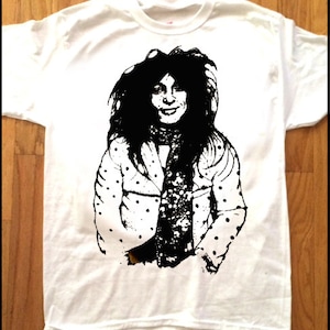 Peut inclure: T-shirt blanc avec une illustration en noir et blanc d'une personne aux cheveux longs portant une chemise à pois et une écharpe.