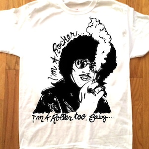 Puede incluir: Camiseta blanca con una ilustración en blanco y negro de una persona con un cigarrillo y el texto "I'm a Rocker... I'm a Roller too, Baby..."