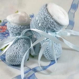 May include: A pair of light blue crocheted baby booties with white cotton lining and blue satin ribbon ties.