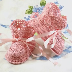 May include: A pair of pink crocheted baby booties with satin ribbon ties. The booties are tied together with the ribbon.