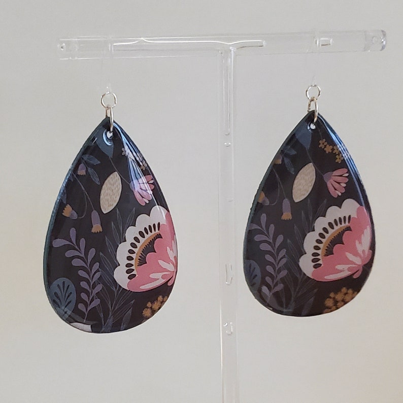 May include: A pair of teardrop-shaped earrings with a floral pattern. The earrings are black with pink, white, and gold accents.