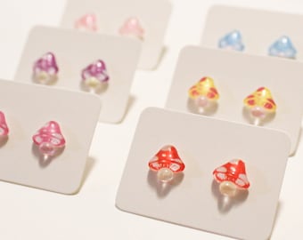 May include: A set of mushroom-shaped earrings in various colors, including pink, purple, yellow, blue, and red. The earrings are displayed on white cards.