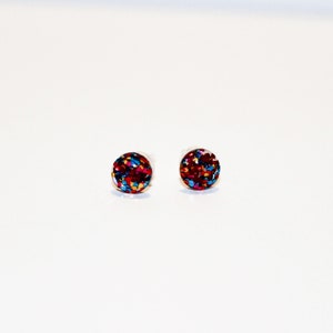 May include: A pair of small, round stud earrings with a red, blue, and gold glitter design.