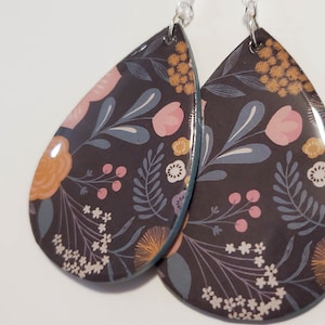 May include: A pair of teardrop-shaped earrings with a floral pattern. The earrings are black with pink, orange, and blue flowers and leaves. The earrings have a silver hook.