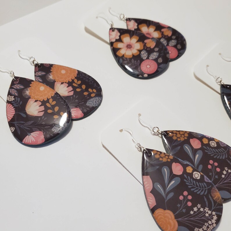 May include: A pair of teardrop-shaped earrings with a floral pattern in shades of pink, orange, and brown on a black background.