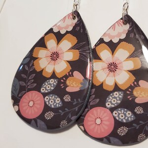 May include: A pair of teardrop-shaped earrings with a floral pattern. The earrings are black with pink, yellow, and white flowers.