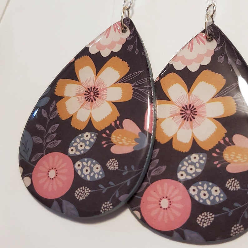 May include: A pair of teardrop-shaped earrings with a floral pattern. The earrings are black with pink, yellow, and white flowers.