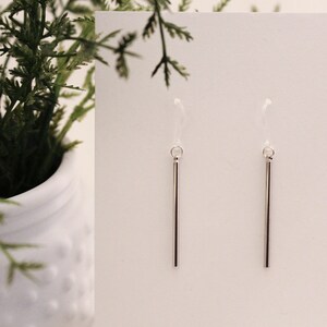 May include: A pair of silver dangle earrings with thin, straight bars hanging from small hoops.