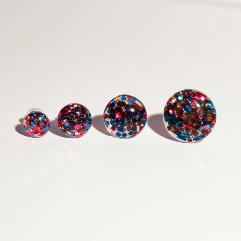 May include: Four round, colorful, glitter-filled earrings in different sizes. The earrings are red, blue, gold, and pink.