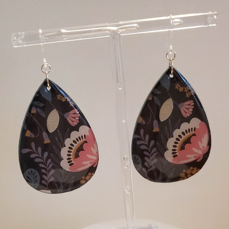 May include: A pair of teardrop-shaped earrings with a floral pattern. The earrings are black with pink, white, and purple flowers and leaves.