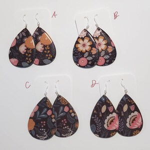 May include: Four pairs of dangle earrings with floral patterns on a black background. The earrings are labeled A, B, C, and D.