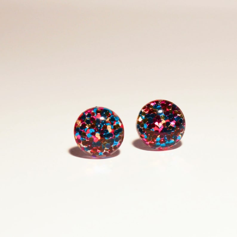 May include: A pair of small, round earrings with a glittery finish. The earrings are red, blue, and gold.