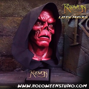 May include: A red latex mask of a skull with a black hooded robe. The mask has a detailed skull design with a red and black color scheme. The mask is on a black stand with the text "Roloween" in gold lettering. The text "LATEX MASKS" is visible in the upper right corner of the image. The text "WWW.ROLOWEENSTUDIO.COM" is visible at the bottom of the image.