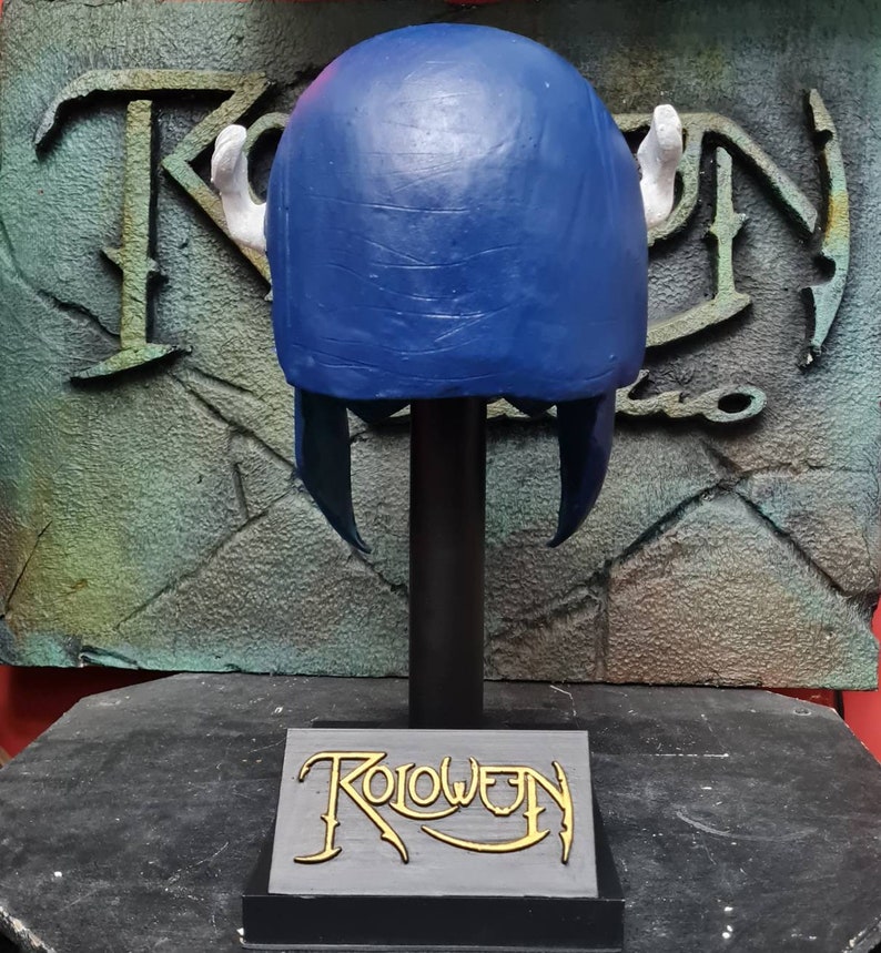 May include: Blue and white helmet with horns on a black stand with the word "Roloween" on the base.