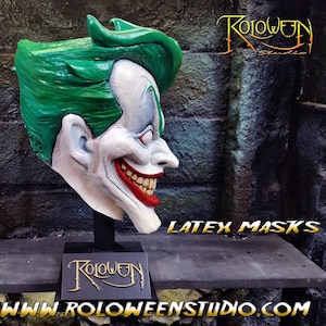 May include: A green and white latex mask of a grinning character with a green mohawk. The mask is on a black stand with the word "Roloween" in gold lettering. The text "LATEX MASKS" is visible in the background. The text "www.roloweenstudio.com" is visible in the foreground.