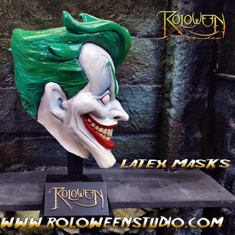 May include: A green and white latex mask of a grinning character with a green mohawk. The mask is on a black stand with the word "Roloween" in gold lettering. The text "LATEX MASKS" is visible in the background. The text "www.roloweenstudio.com" is visible in the foreground.