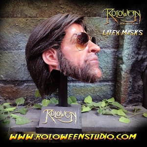 May include: A realistic latex mask of a man with brown hair and a beard, wearing sunglasses. The mask is on a black stand with the word "Roloween" in gold lettering. The text "LATEX MASKS" is visible in the upper right corner of the image. The website address "www.roloweenstudio.com" is visible at the bottom of the image.